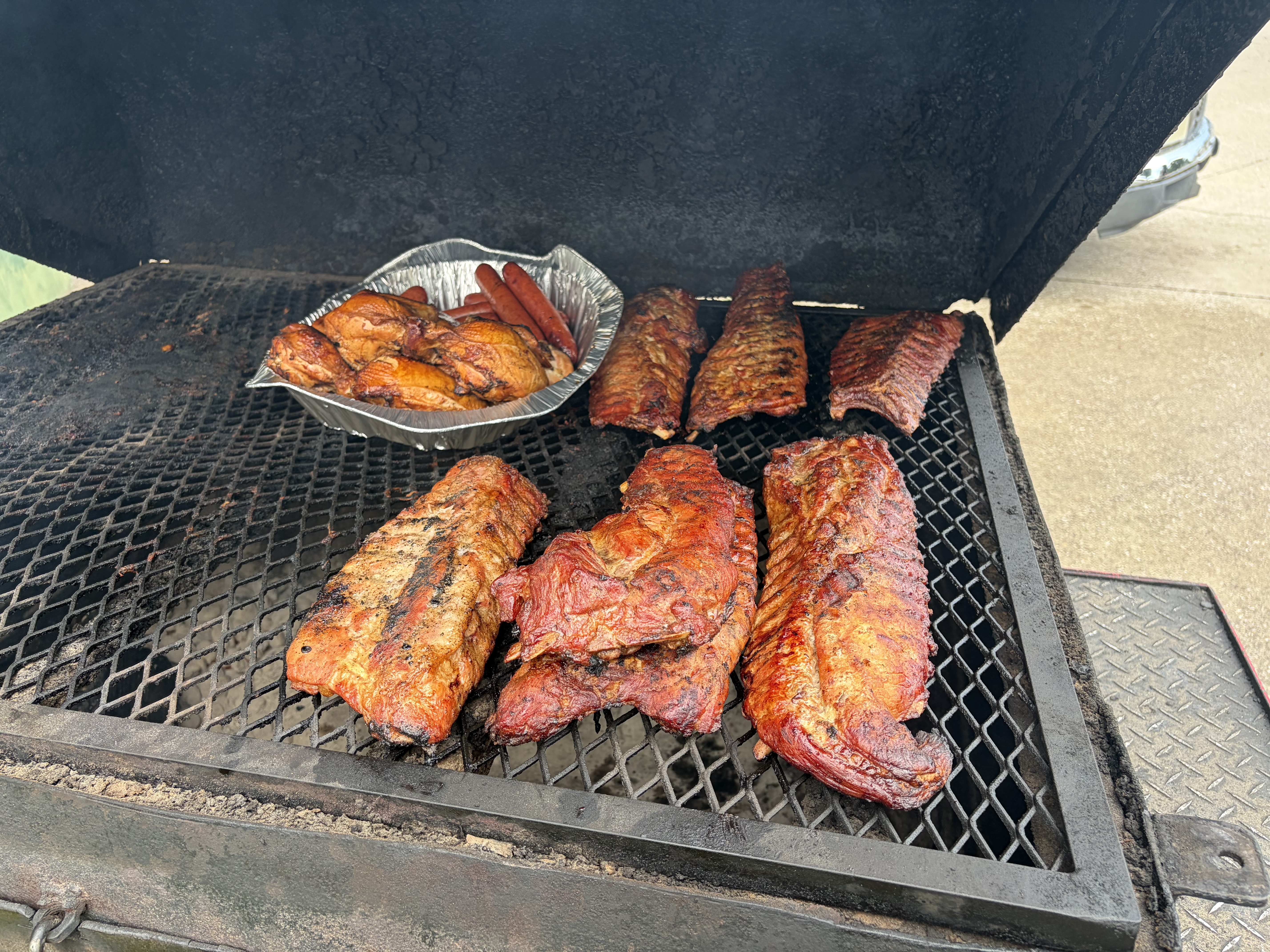 Racks of ribs, smoked chicken and hot links laid out on an open offset smoker